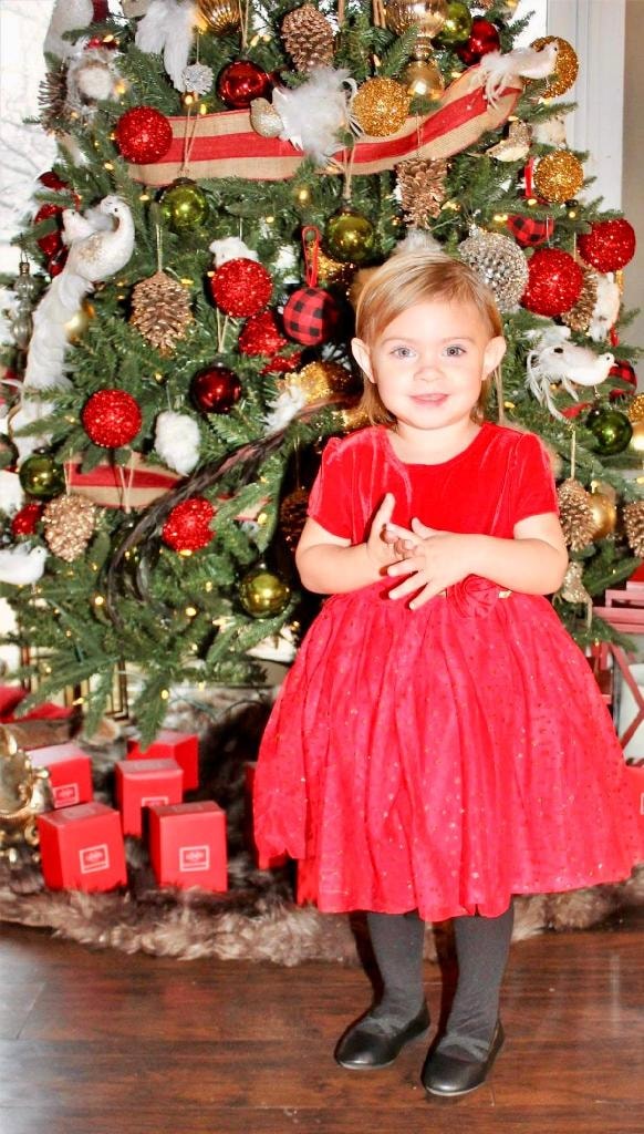 Little girl in red dress by Christmas tree at Kiddie Care